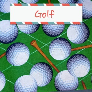 May include: Green fabric with a repeating pattern of white golf balls and brown golf tees. The fabric has the word "Golf" printed on it.