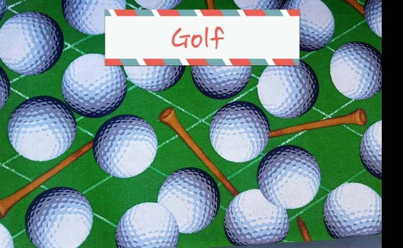 May include: Green fabric with a repeating pattern of white golf balls and brown golf tees. The fabric has the word "Golf" printed on it.