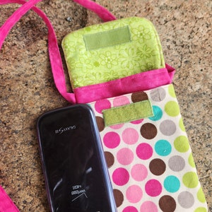 May include: A pink and green fabric phone case with a polka dot pattern and a flap closure. The case has a strap for carrying over the shoulder. A black Samsung Galaxy S III phone is inside the case.