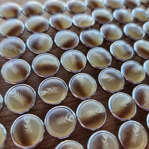 May include: A close-up of a large collection of small, round, silver-rimmed, decorative objects with a brown and white pattern. The objects are arranged in a grid pattern on a wooden surface.