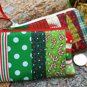 May include: Two Christmas-themed zippered pouches. One features green fabric with white polka dots, candy canes, and red stripes. The other has a Christmas tree design and plaid fabric. Both have red zippers and white lining.