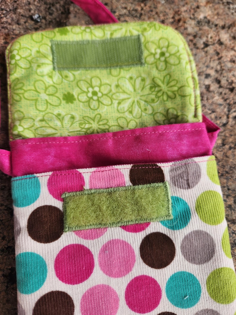 May include: A pink and white fabric bag with brown, pink, and turquoise polka dots. The bag has a green fabric flap with a velcro closure.