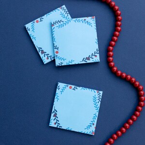 May include: Three blue notepads with a floral design and red berries. The notepads are on a dark blue background. A red beaded necklace is in the background.