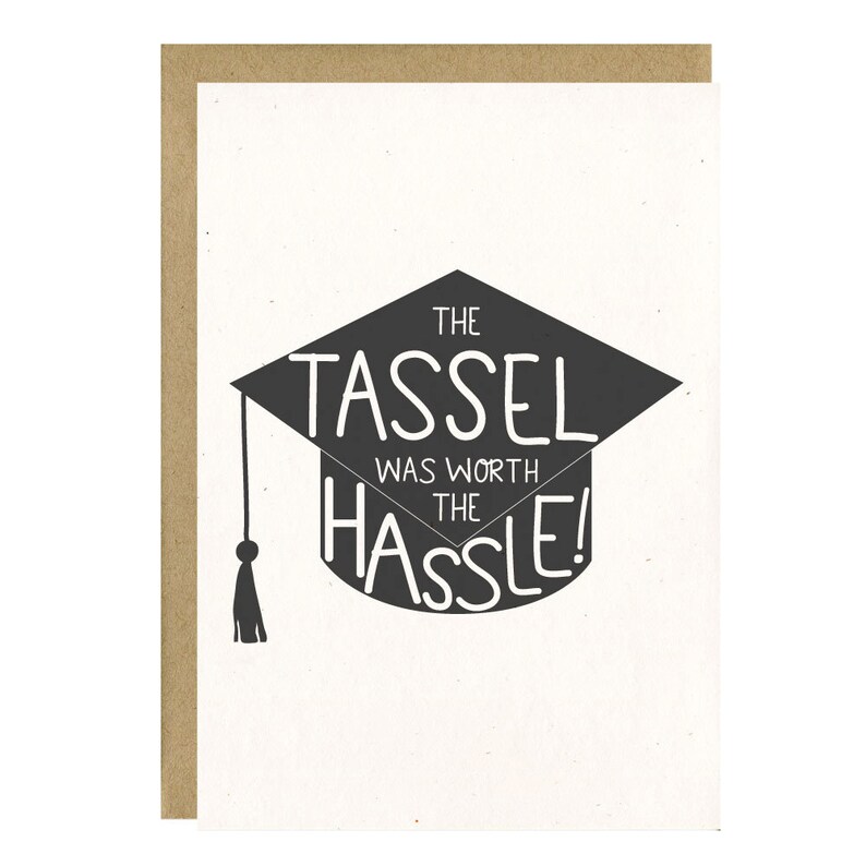 May include: A graduation card with a white background and a brown border. The card features a black graduation cap graphic with the text "THE TASSEL WAS WORTH THE HASSLE!" in white, celebrating academic achievement.