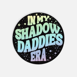 May include: A black circle sticker with a rainbow gradient design. The text "In My Shadow Daddies Era" is written in a retro font style.