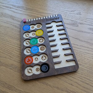 May include: A wooden game board with a round track for tokens and a separate section labeled "Initiative". The board has slots for tokens and a black marker. The board is made of dark wood with a light wood inlay.