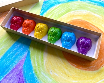 May include: A set of six colorful ladybug-shaped crayons in a cardboard box. The crayons are arranged in a rainbow order, starting with red and ending with purple.