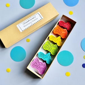 May include: A set of six rainbow-colored motorcycle-shaped crayons in a cardboard box. The crayons are arranged in a row, with the red crayon at the top and the purple crayon at the bottom. The box has a label that says "Kraftedaway" and "Motorcycle Crayons".