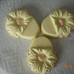 May include: Three yellow ceramic flower-shaped soap dishes with pink hearts in the center of each flower. The dishes are on a white surface.