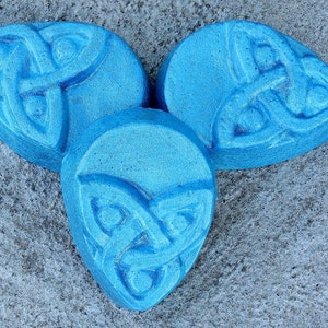 May include: Three blue bath bombs shaped like a Celtic knot. The bath bombs are on a gray textured surface.
