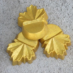 May include: Three gold-colored acorn-shaped ornaments with leaf details. The ornaments are arranged in a cluster on a gray surface.