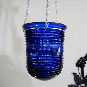 May include: A blue glass hanging lantern with a ribbed design. The lantern is suspended from a silver chain.