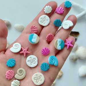 May include: A collection of colorful and white sea-themed polymer clay earrings. The earrings feature seashells, starfish, sand dollars, and ocean waves.