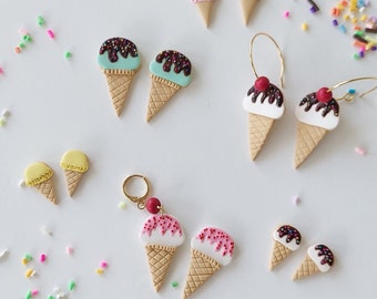 May include: A collection of ice cream cone earrings and studs in various colors. The earrings feature gold hoops and red cherry accents. The ice cream cones have brown waffle cones and colorful sprinkles.