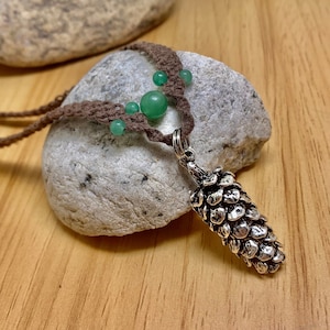 May include: A brown cord necklace with a silver pine cone pendant and green jade beads.