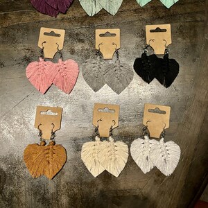 May include: Nine pairs of handmade tassel earrings in various colors, including pink, purple, green, gray, black, white, and brown. The earrings are displayed on individual cards with a simple design.