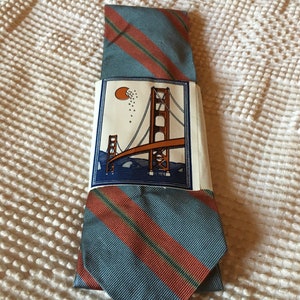 Puede incluir: Una corbata a rayas azules y naranjas con una etiqueta que muestra un dibujo del Puente Golden Gate en San Francisco.