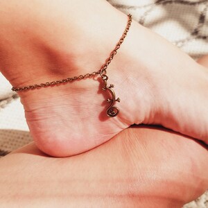 May include: A gold anklet with a lizard charm. The anklet is on a person's ankle.