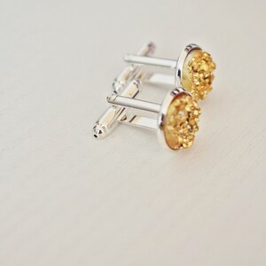 May include: A pair of silver cufflinks with gold-colored, textured, oval-shaped faces. The cufflinks are set against a white background, showcasing their metallic shine and intricate details. These accessories are suitable for formal wear.