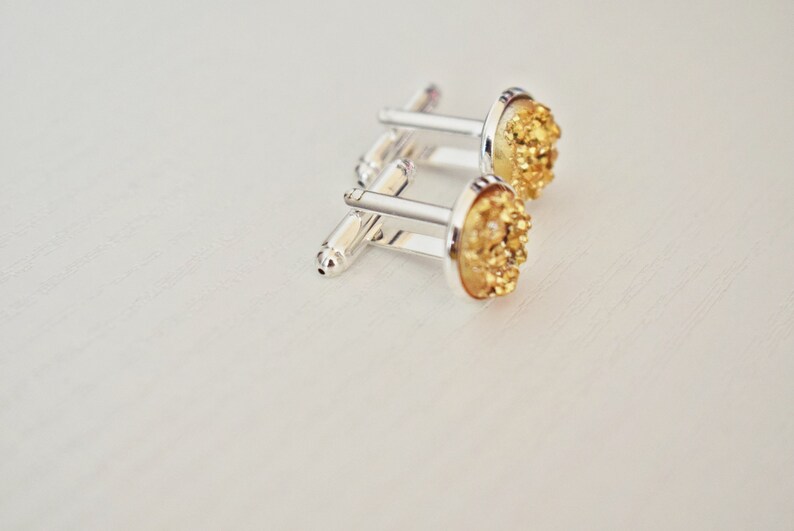 May include: A pair of silver cufflinks with gold-colored, textured, oval-shaped faces. The cufflinks are set against a white background, showcasing their metallic shine and intricate details. These accessories are suitable for formal wear.