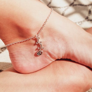 May include: A silver ankle bracelet with a delicate chain and a charm shaped like a stylized lizard.