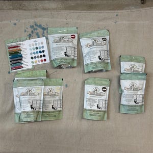 May include: A collection of eight unopened bags of milk paint. The bags are green and white with the words "Milk Paint" printed on them. The bags are arranged in two rows of four.