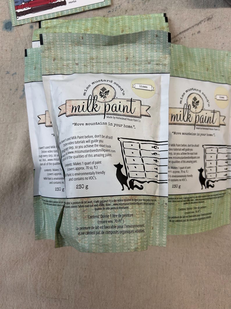 May include: A bag of Miss Mustard Seed's Milk Paint in the color Linen. The bag is white with green and yellow accents. The text on the bag reads "Miss Mustard Seed's Milk Paint" and "Move mountains in your home." The bag also includes information about the paint, such as the coverage and the fact that it is environmentally friendly and contains no VOCs.