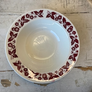 May include: A white ceramic bowl with a red floral design around the rim. The bowl is empty and has a slight shine.