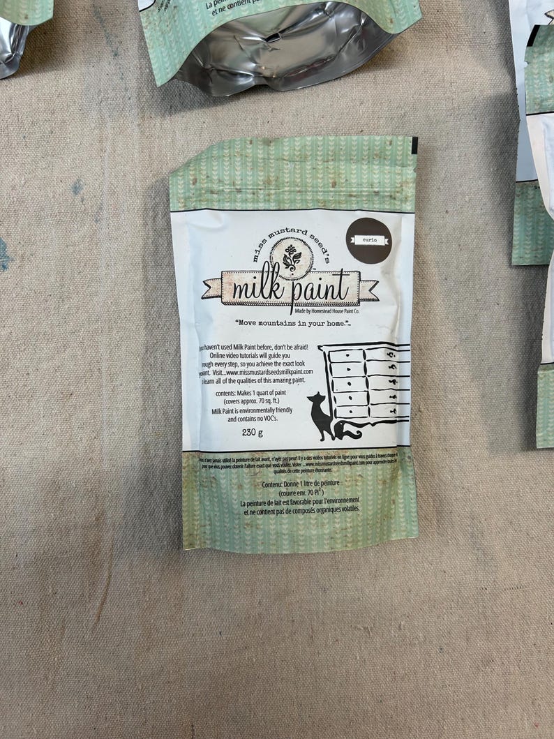 May include: A 230 gram bag of Mustard Seed's Milk Paint in the color "Marigold". The bag is white with green and brown accents. The text "Move mountains in your home." is printed on the bag.
