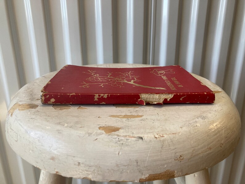 Peut inclure: Un livre reli&eacute; rouge avec une inscription dor&eacute;e sur le dos qui dit "The Year in My Garden". Le livre est pos&eacute; sur un tabouret blanc.