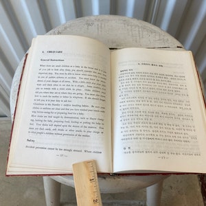Peut inclure: Un livre ouvert avec une couverture rouge et des pages blanches. Le livre est intitul&eacute; "Child Care" et contient une section sur les instructions g&eacute;n&eacute;rales. Le livre est pos&eacute; sur une surface blanche avec une r&egrave;gle &agrave; c&ocirc;t&eacute;.