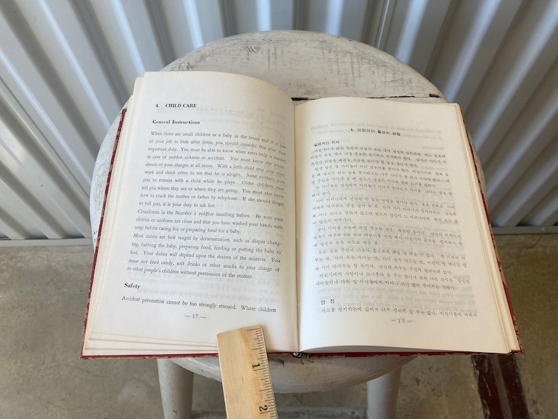 Peut inclure: Un livre ouvert avec une couverture rouge et des pages blanches. Le livre est intitul&eacute; "Child Care" et contient une section sur les instructions g&eacute;n&eacute;rales. Le livre est pos&eacute; sur une surface blanche avec une r&egrave;gle &agrave; c&ocirc;t&eacute;.