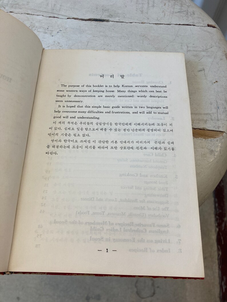 Peut inclure: Une page d'un livre vintage avec une page de titre qui lit "머리말" en cor&eacute;en. Le texte est en cor&eacute;en et en anglais et explique le but du livre, qui est d'aider les domestiques cor&eacute;ens &agrave; comprendre les fa&ccedil;ons occidentales de tenir une maison.