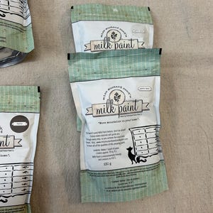 May include: Three bags of Miss Mustard Seed's Milk Paint. The bags are green with white polka dots and feature a vintage-style logo. The text on the bags reads "Miss Mustard Seed's Milk Paint" and "Move mountains in your home."