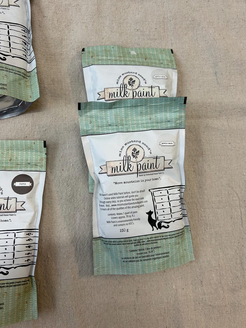 May include: Three bags of Miss Mustard Seed's Milk Paint. The bags are green with white polka dots and feature a vintage-style logo. The text on the bags reads "Miss Mustard Seed's Milk Paint" and "Move mountains in your home."