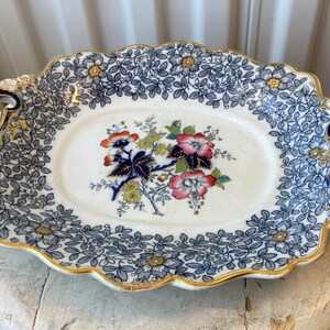 May include: A white oval serving dish with blue and gold floral designs and blue and gold handles.