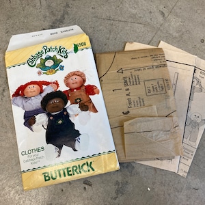 May include: A vintage sewing pattern for Cabbage Patch Kids clothes. The pattern is for a shirt and includes instructions for making the garment. The pattern is from the brand Butterick and has the number 6508.