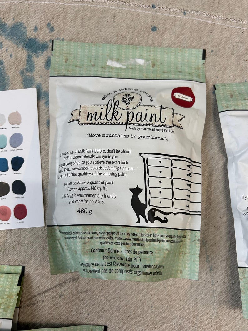 May include: A bag of Miss Mustard Seed's Milk Paint in the color Eclipse. The bag is white with green and black text. The text on the bag reads "Miss Mustard Seed's Milk Paint" and "Move mountains in your home." The bag also includes the text "Made by Homestead House Paint Co."