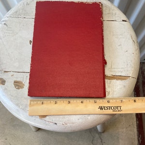 Peut inclure: Un livre reli&eacute; rouge avec une couverture unie. Le livre est pos&eacute; sur un tabouret blanc avec une r&egrave;gle en bois en dessous.