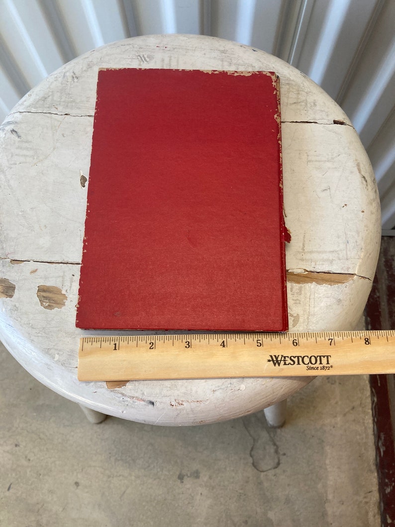Peut inclure: Un livre reli&eacute; rouge avec une couverture unie. Le livre est pos&eacute; sur un tabouret blanc avec une r&egrave;gle en bois en dessous.