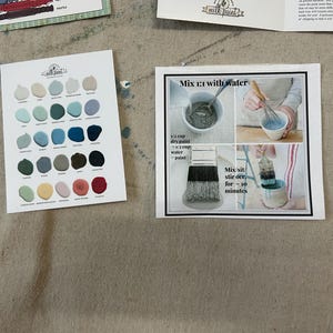May include: A color chart with 36 paint colors, including blues, greens, grays, and reds. The chart is labeled "Milk Paint". A separate card shows instructions for mixing the paint with water, using a 1:1 ratio of dry paint to water. The instructions also state to mix and stir for 10 minutes.
