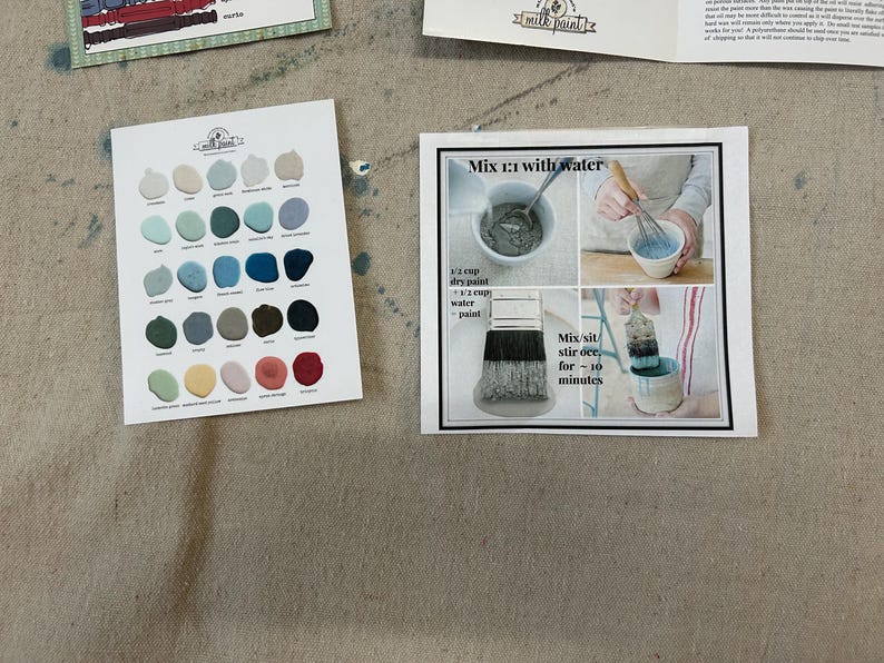 May include: A color chart with 36 paint colors, including blues, greens, grays, and reds. The chart is labeled "Milk Paint". A separate card shows instructions for mixing the paint with water, using a 1:1 ratio of dry paint to water. The instructions also state to mix and stir for 10 minutes.