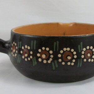 May include: A brown ceramic fondue pot with a handle and a decorative floral design in white, brown, and green.