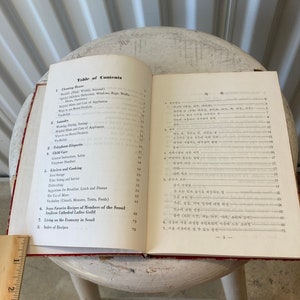Peut inclure: Un livre rouge et blanc avec une table des mati&egrave;res pour un guide de vie &agrave; S&eacute;oul, en Cor&eacute;e du Sud. Le livre comprend des sections sur le nettoyage, la lessive, l'&eacute;tiquette t&eacute;l&eacute;phonique, la garde d'enfants, la cuisine et la cuisine, les recettes et la vie avec un budget &agrave; S&eacute;oul.