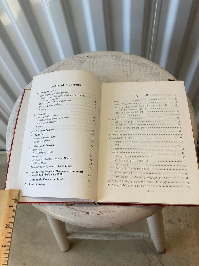 Peut inclure: Un livre rouge et blanc avec une table des mati&egrave;res pour un guide de vie &agrave; S&eacute;oul, en Cor&eacute;e du Sud. Le livre comprend des sections sur le nettoyage, la lessive, l'&eacute;tiquette t&eacute;l&eacute;phonique, la garde d'enfants, la cuisine et la cuisine, les recettes et la vie avec un budget &agrave; S&eacute;oul.