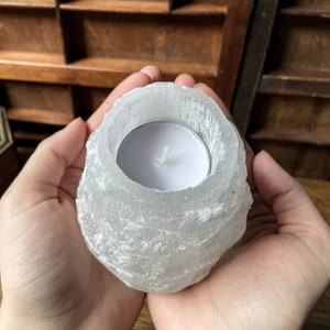 Puede incluir: Un portavelas de sal del Himalaya blanco con una pequeña vela de té blanca en su interior. El portavelas tiene la forma de una roca natural rugosa.