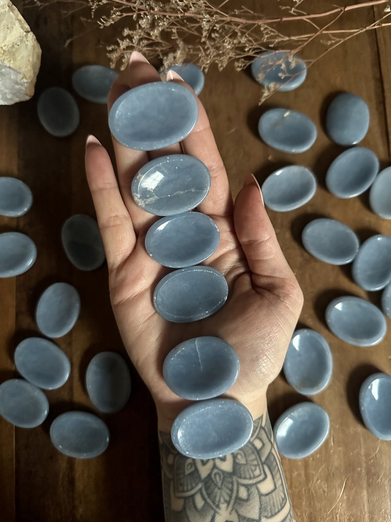 May include: A collection of smooth, light blue, oval-shaped stones. The stones are arranged in a pattern on a wooden surface.