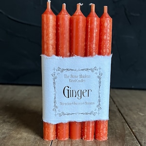 K&ouml;nnte beinhalten: Eine Packung mit sechs orangefarbenen Ritualkerzen mit der Aufschrift "The Stone Maidens Ritual Candles Ginger Attraction + Success + Ambition".