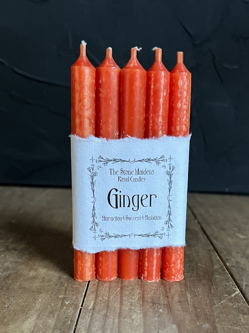 K&ouml;nnte beinhalten: Eine Packung mit sechs orangefarbenen Ritualkerzen mit der Aufschrift "The Stone Maidens Ritual Candles Ginger Attraction + Success + Ambition".