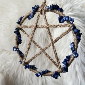 May include: A handmade dreamcatcher with a brown jute rope base and a five-pointed star design. The dreamcatcher is decorated with a circle of blue lapis lazuli stones.